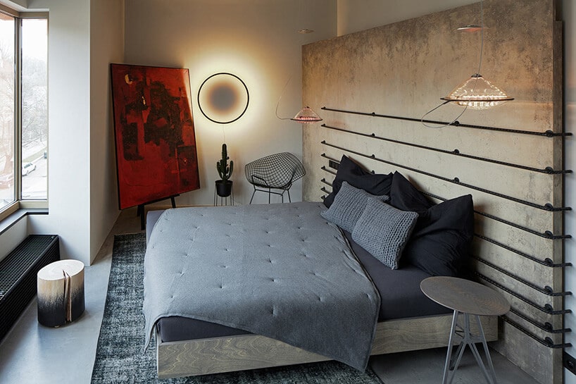 sypialnia industrialna z dużym łóżkiem oraz zagłowkiem w kolorze szarym oraz wiszący na ścianie okrąg świecący'