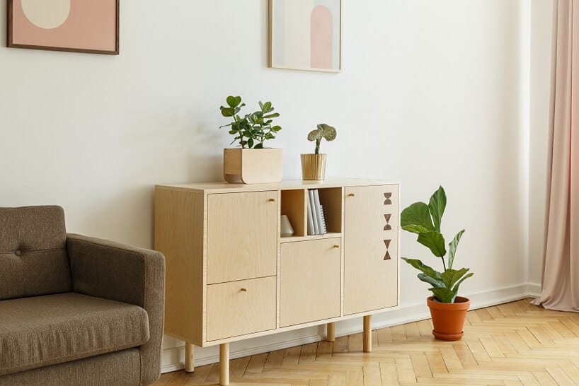 drewnianana komoda brązowa sofa na tle białej ściany z różowo żóltymi obrazami i drewnianą podłogą