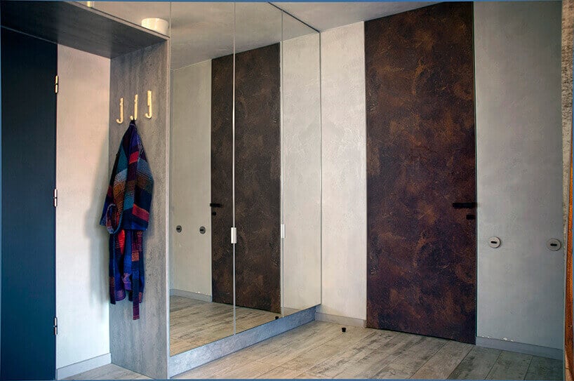 przedpokój z wysokimi drzwiami pokrytymi rdzą przy kremowej ścianie z lustrem