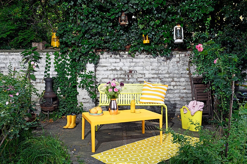 żółte nowoczesne meble ogrodowe ławka i stoli na tle białego starego murku