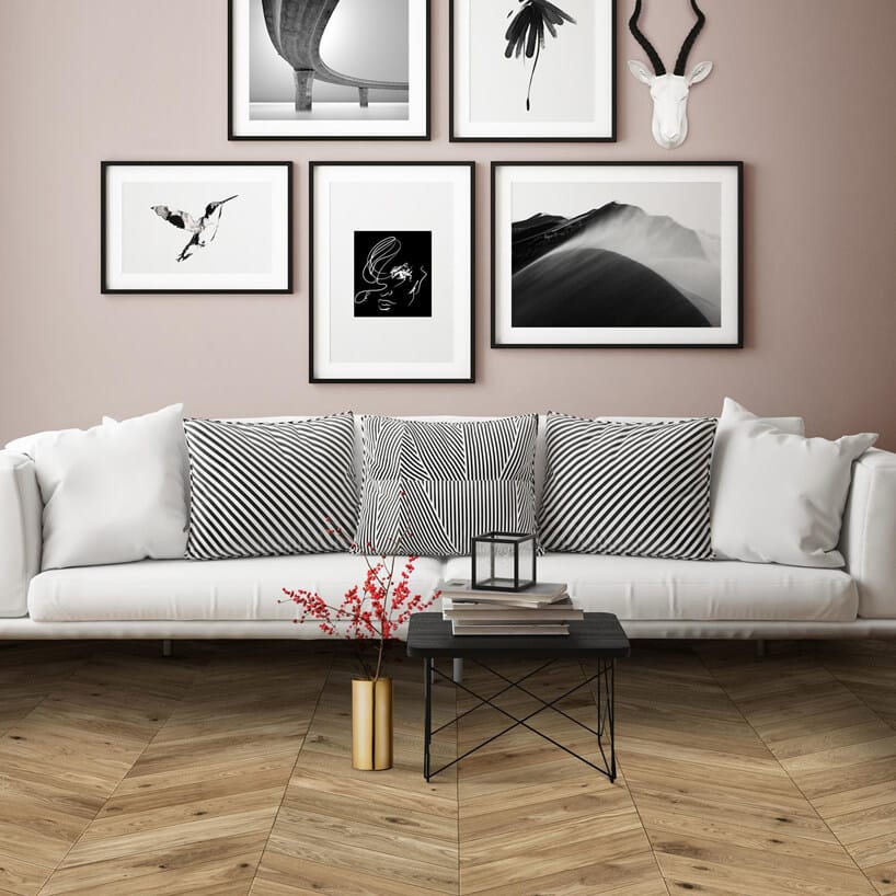 duża biała sofa na drewnianej podłodze na tle beżowej ściany z obrazami