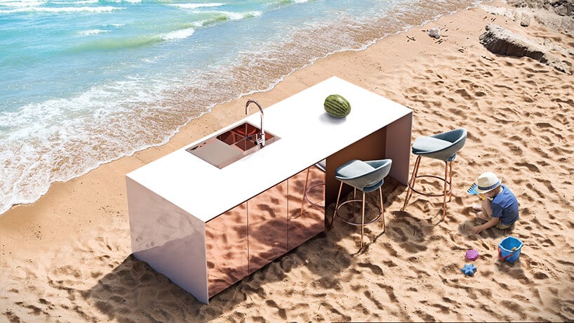 kuchnia z połyskującym panele z różem oraz białym blatem na plaży przy morzu i falach