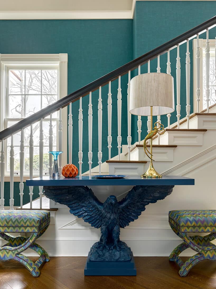 niebieski stół z podstawą w kształcie orła z rozłożonymi skrzydłami na tle biało-brązowych schodów