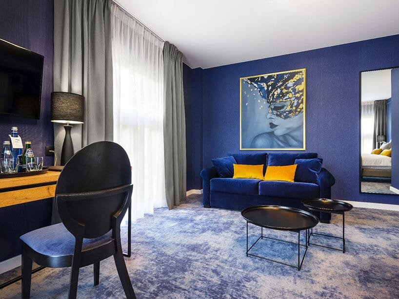 Wawel Queen pokój hotelowy z niebieską kanapą i ścianą, obrazem i żółtymi poduszkami